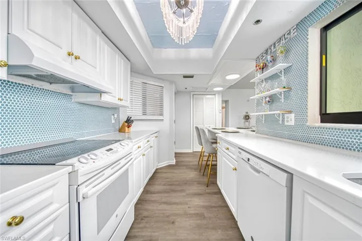 Kitchen with white cabinets, white appliances, a tray ceiling, and blue backsplash tile.