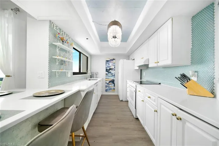 Galley style kitchen with granite countertops, tile backsplash and a tray ceiling.