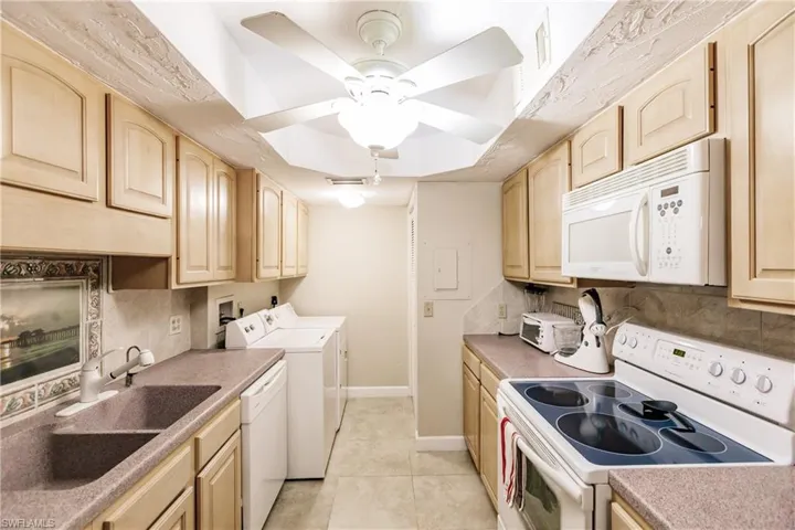 Kitchen with washer and dryer, light brown cabinetry, tasteful backsplash, light tile patterned floors, and white appliances