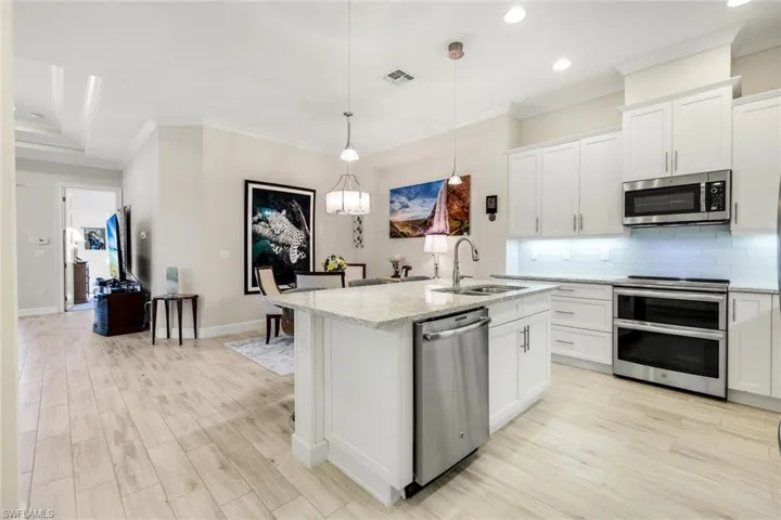 Kitchen with stainless steel appliances, white cabinets, backsplash, decorative light fixtures, and recessed lighting