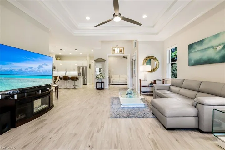 Living area featuring light wood-style flooring, a ceiling fan, recessed lighting, a raised ceiling, and crown molding