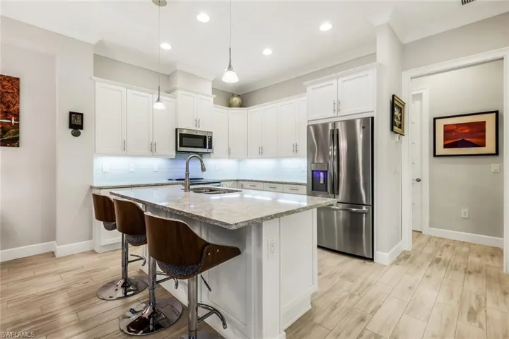Kitchen with backsplash, stainless steel appliances, light stone counters, white cabinetry, and a center island with sink