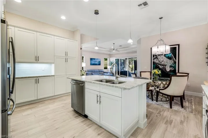 Kitchen featuring white cabinetry, a center island with sink, ceiling fan, open floor plan, and light wood-style floors