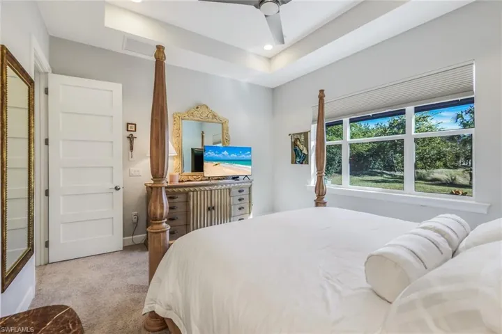 Carpeted bedroom with a ceiling fan, a raised ceiling, and recessed lighting