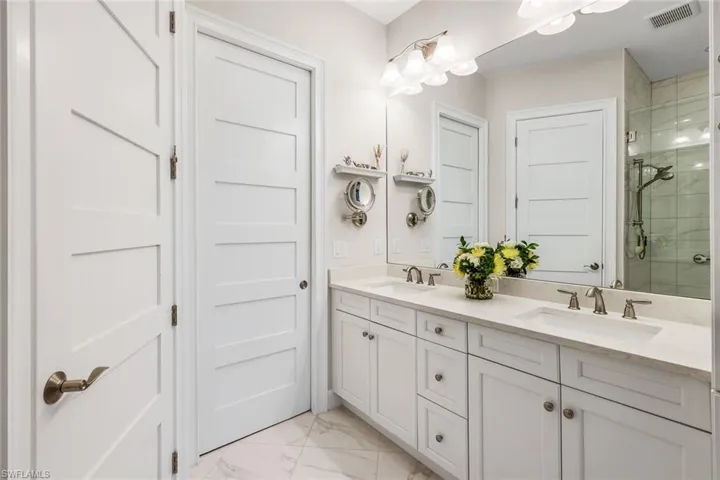 Full bath with double vanity, a stall shower, and light marble finish flooring
