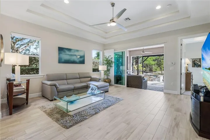Living room with light wood finished floors, a ceiling fan, a tray ceiling, and recessed lighting