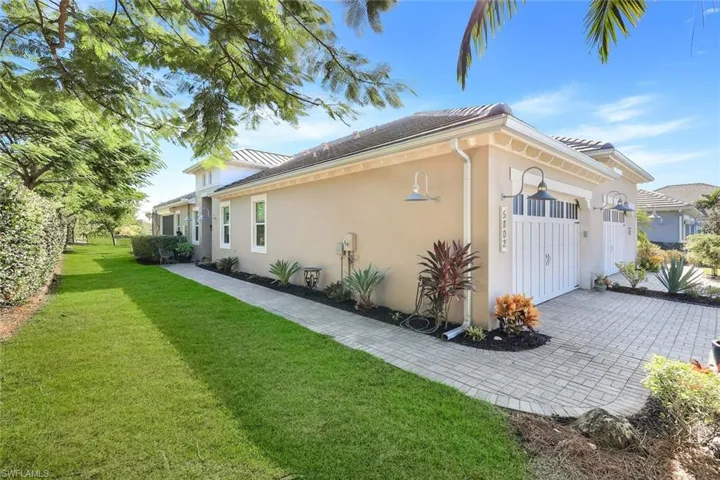 View of side of home with a yard, an attached garage, stucco siding, and decorative driveway