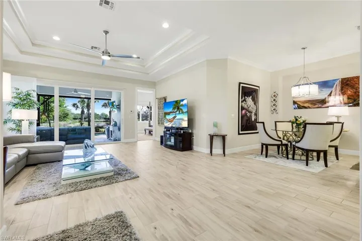 Living room featuring ornamental molding, light wood finished floors, ceiling fan, recessed lighting, and a raised ceiling