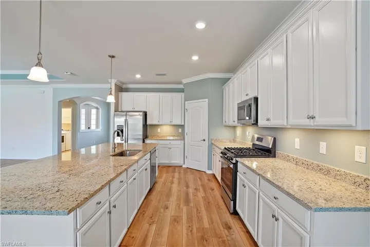 Kitchen featuring pendant lighting, ornamental molding, white cabinetry, appliances with stainless steel finishes, and light hardwood / wood-style floors