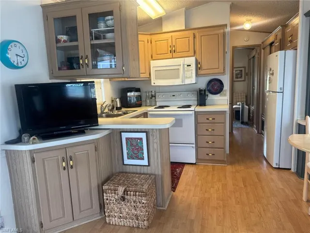 Kitchen with glass insert cabinets, white appliances, vaulted ceiling, light countertops, and light wood finished floors
