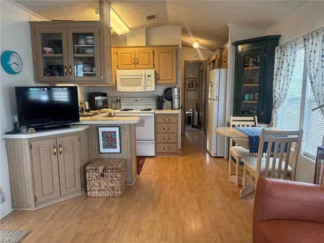 Kitchen featuring visible vents, glass insert cabinets, white appliances, vaulted ceiling, and light wood-style flooring