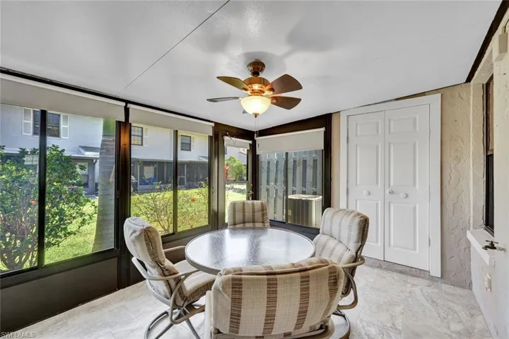Enclosed patio featuring light-toned flooring, expansive windows with roller shades, and a ceiling fan with integrated lighting