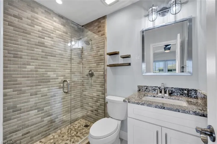Contemporary bathroom featuring a glass-enclosed shower with horizontal brick-patterned tile, pebble-finish shower pan, and brushed nickel fixtures