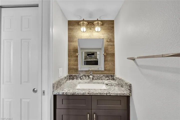 Vanity area featuring a wood-look accent wall, brass-toned wall sconces, a framed mirror, a built-in sink with a countertop, and dark wood-finish cabinetry