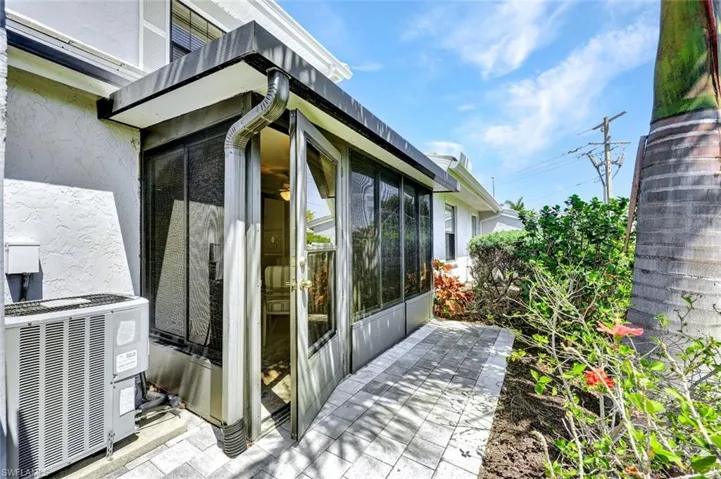 Screened enclosure with dual French doors, a stone paver patio, and mature landscaping