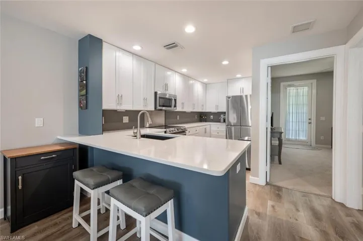 Remodeled kitchen featuring white cabinets, breakfast nook, SS appliances, light wood-type flooring, with a view of first floor bedroom.
