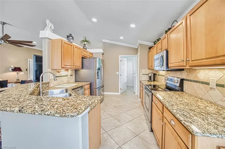 Kitchen featuring stainless steel appliances, a peninsula, light stone counters, vaulted ceiling, and light tile patterned flooring