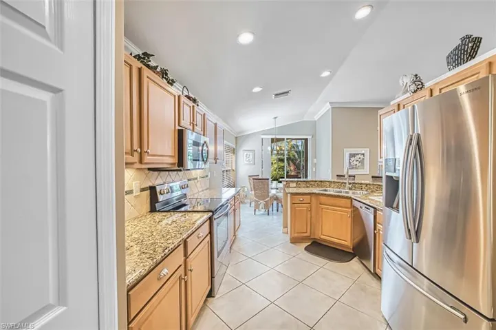Kitchen featuring stainless steel appliances, light stone countertops, lofted ceiling, crown molding, and a peninsula