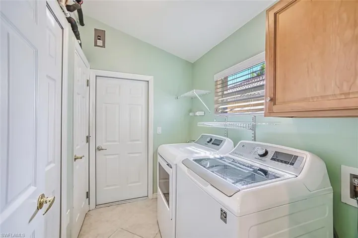 Washroom featuring lofted ceiling, washer and clothes dryer, light tile patterned flooring, and cabinet space