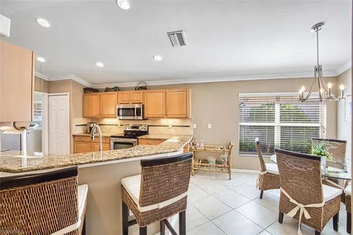 Kitchen with appliances with stainless steel finishes, crown molding, a chandelier, a breakfast bar, and hanging light fixtures