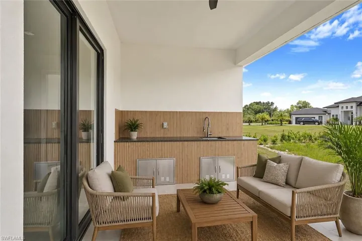 Covered outdoor kitchen featuring a dark countertop, stainless steel sink with a gooseneck faucet, and slatted wood-finish paneling