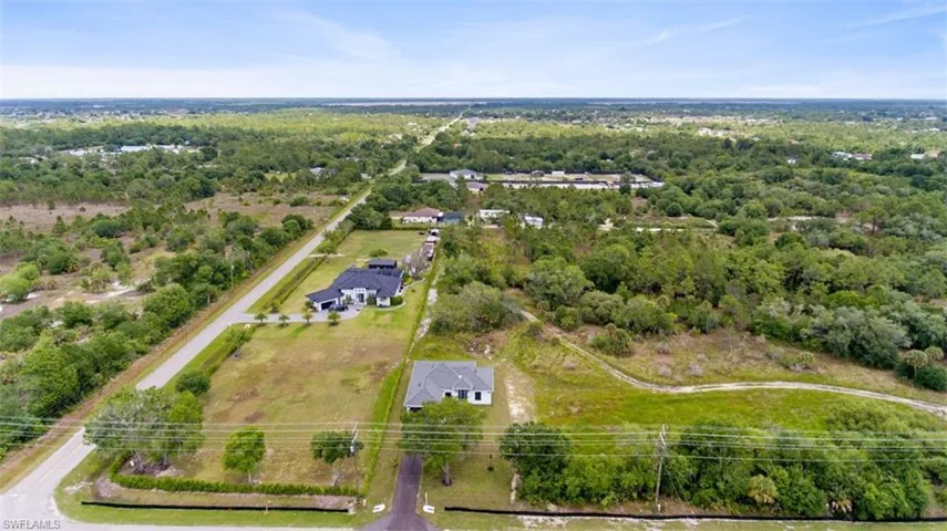Aerial perspective showcasing a modern residence with a dark roofline, set on a sizable property with a paved driveway
