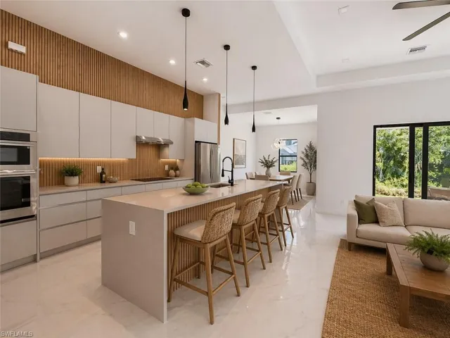 Open-concept living space featuring a gourmet kitchen with integrated appliances, a large center island with seating, a wood-slat accent wall, and recessed lighting