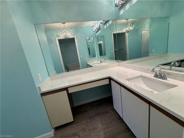 Full bath featuring double vanity, dark wood-style floors, and a chandelier