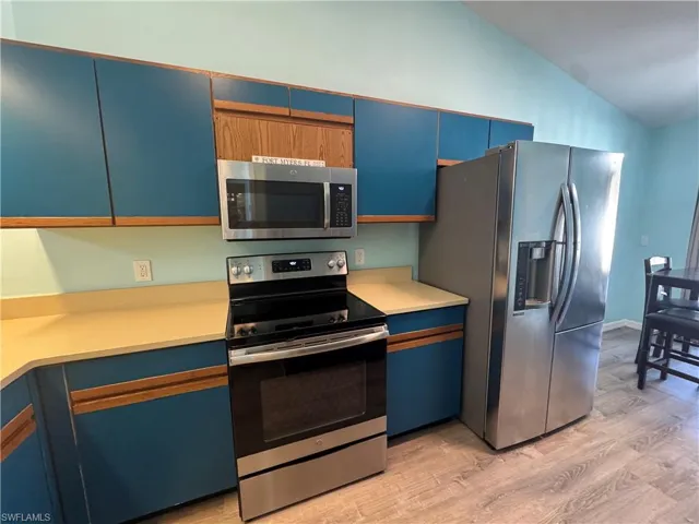 Kitchen with blue cabinets, stainless steel appliances, light wood finished floors, light countertops, and vaulted ceiling