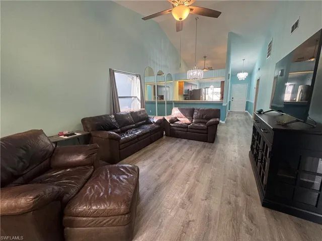 Living area featuring high vaulted ceiling, wood finished floors, healthy amount of natural light, a ceiling fan, and a chandelier