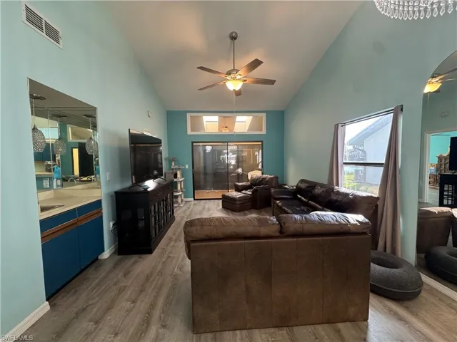 Living room with high vaulted ceiling, light wood finished floors, and ceiling fan