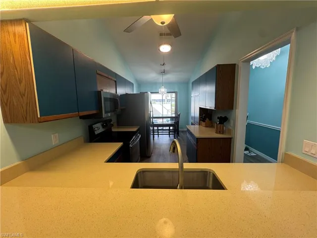 Kitchen featuring black appliances, lofted ceiling, ceiling fan, wood finished floors, and decorative light fixtures