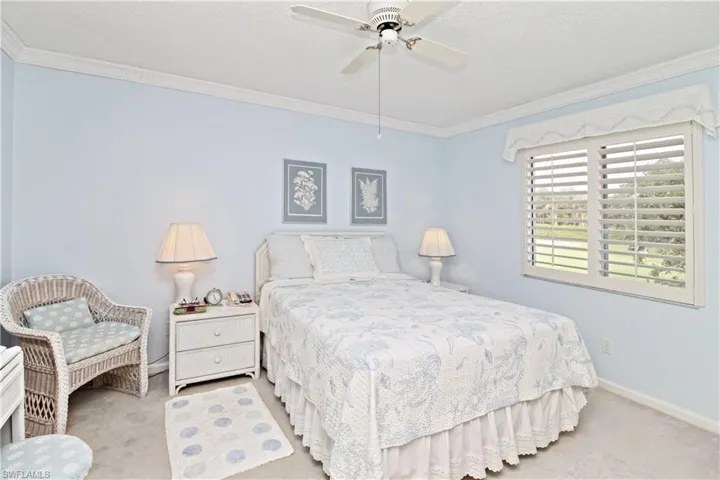 Golf course view from primary bedroom with plantation shutters and crown molding.