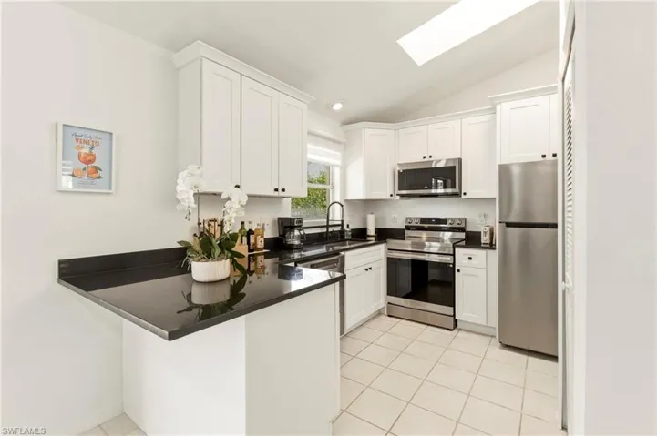 Kitchen featuring stainless steel appliances, white cabinetry, a skylight, vaulted ceiling, and a peninsula