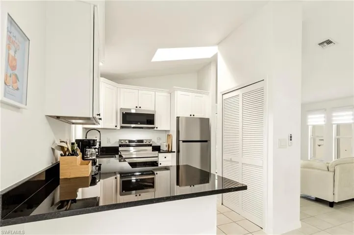 Kitchen with white cabinets, stainless steel appliances, vaulted ceiling, a skylight, and light tile patterned floors