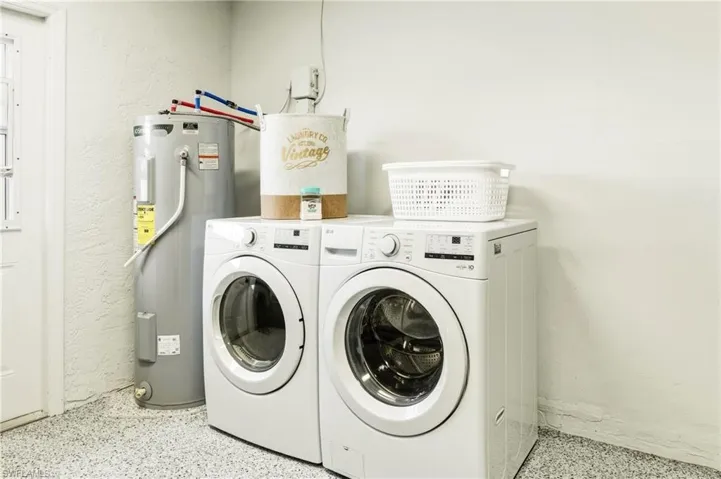 Laundry area featuring electric water heater, a textured wall, dark speckled floor, and separate washer and dryer