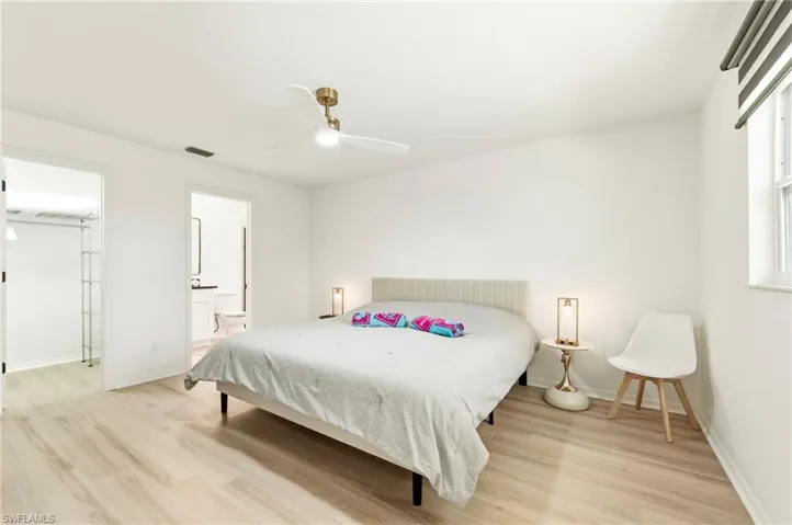 Bedroom with light wood-style flooring, ceiling fan, and ensuite bath