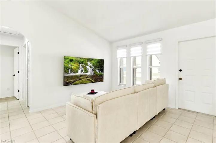 Living room with lofted ceiling, light tile patterned flooring, and arched walkways