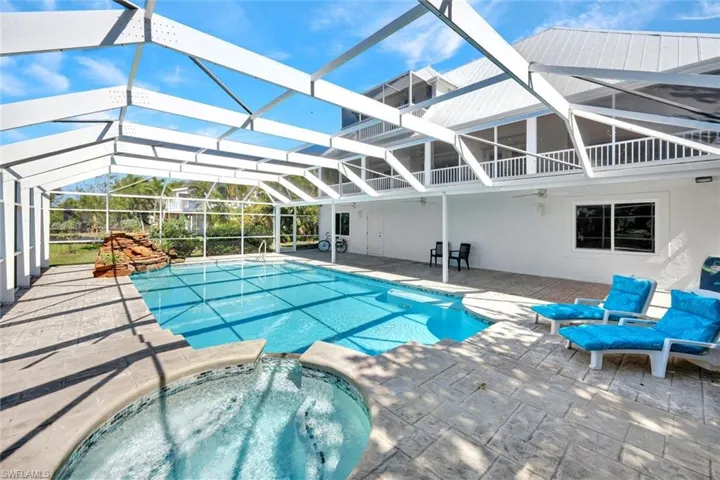 Screened-in pool area featuring a rectangular swimming pool, integrated hot tub with mosaic tile accents, and a rock waterfall feature