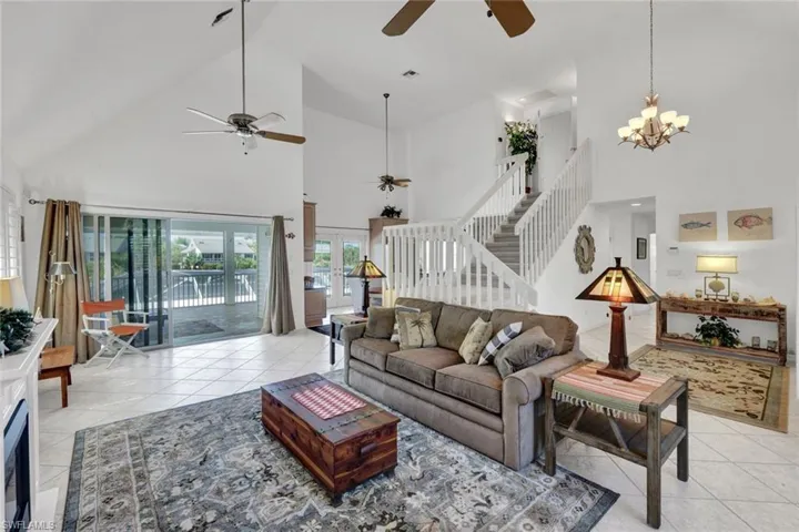 Vaulted ceilings accentuating a spacious interior with large sliding glass doors, tile flooring, a staircase with white railings, and a built-in fireplace