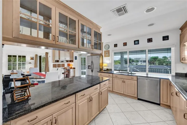 Light wood-finish cabinetry throughout featuring upper glass-front cabinets and dark stone countertops