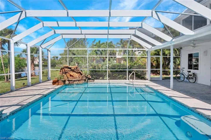 Screen-enclosed swimming pool featuring a rock waterfall, concrete deck, and pool steps