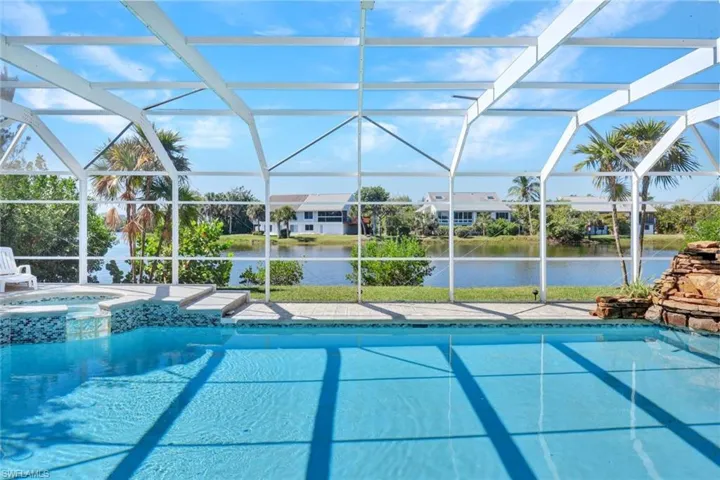 Screened pool enclosure featuring a large pool, integrated spa, and a natural stone-look waterfall structure