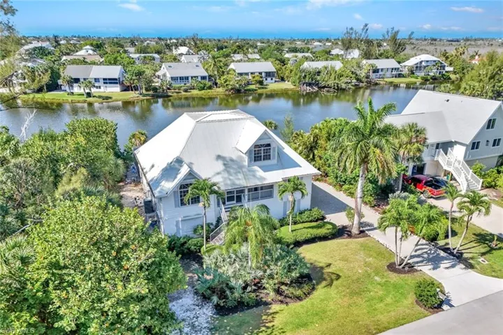 Waterfront property featuring a metal roof, mature tropical landscaping, a private driveway, and a waterside patio area