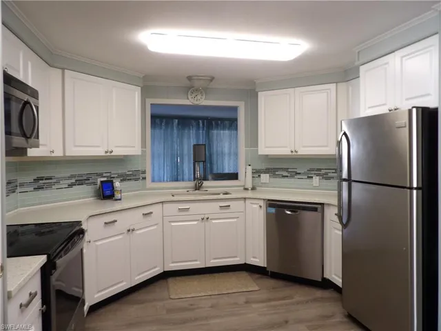 Kitchen featuring stainless steel appliances, white cabinets, luxury vinyl floors, ornamental molding, and light quartz counters