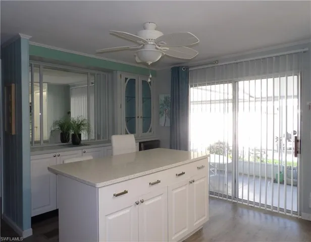 Kitchen with white cabinets, quartz counters, a ceiling fan, a kitchen island, wine refrigerator and crown molding