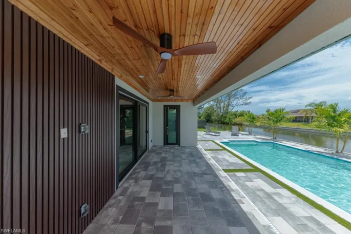 Outdoor pool with a patio, a ceiling fan, and a water view