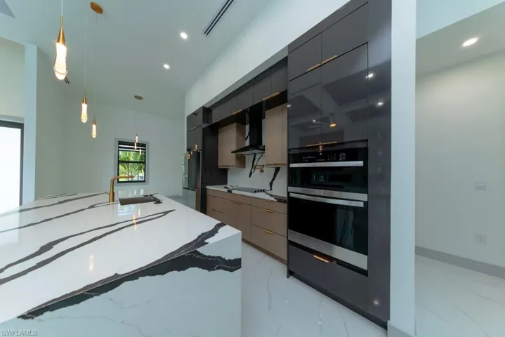 Kitchen featuring modern cabinets, wall chimney exhaust hood, double oven, hanging light fixtures, and recessed lighting