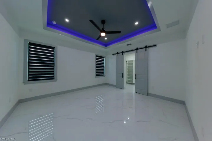 Empty room with light marble finish floors, a barn door, a raised ceiling, ceiling fan, and recessed lighting
