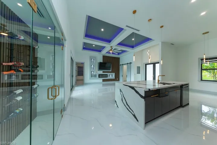 Kitchen featuring modern cabinets, light marble finish flooring, coffered ceiling, a center island with sink, and stainless steel dishwasher